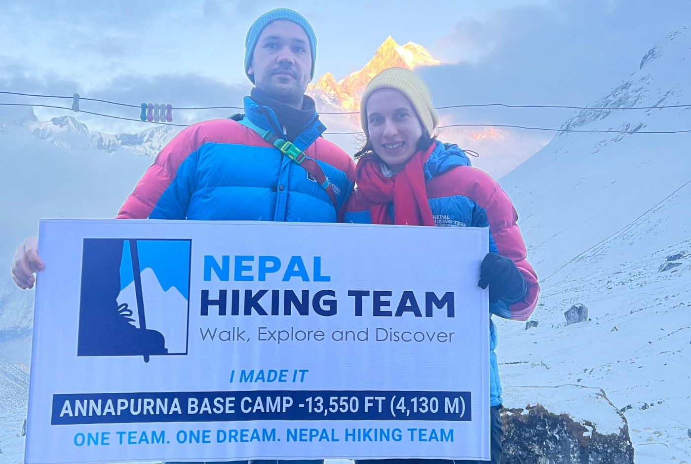 Trekkers holding Nepal Hiking Team sign at Annapurna Base Camp with snowy Annapurna views