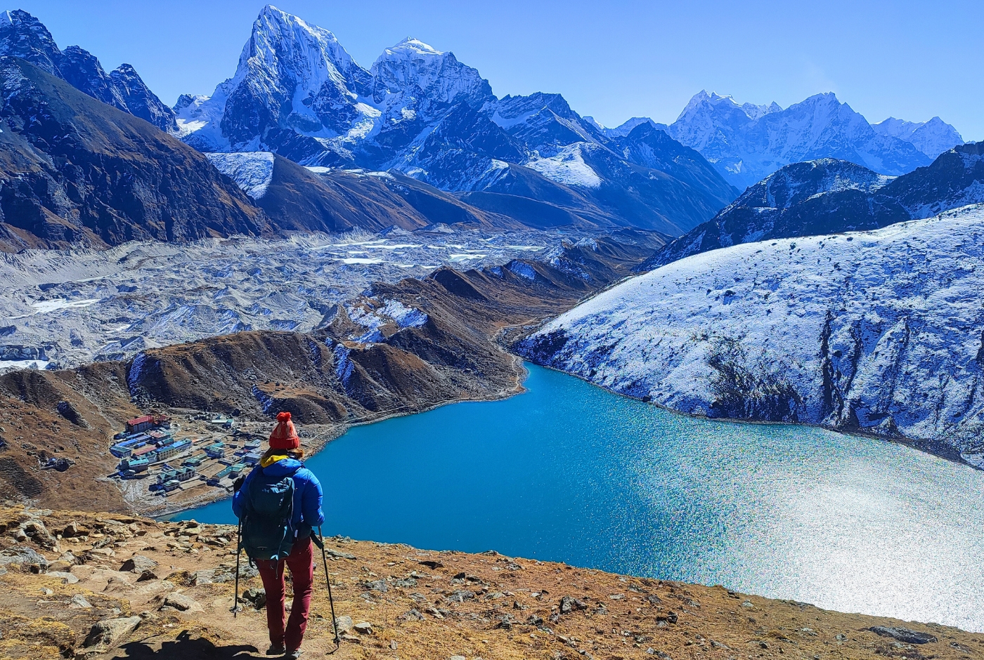 A hiker overlooking Gokyo Lake in Nepal, surrounded by snowy mountains