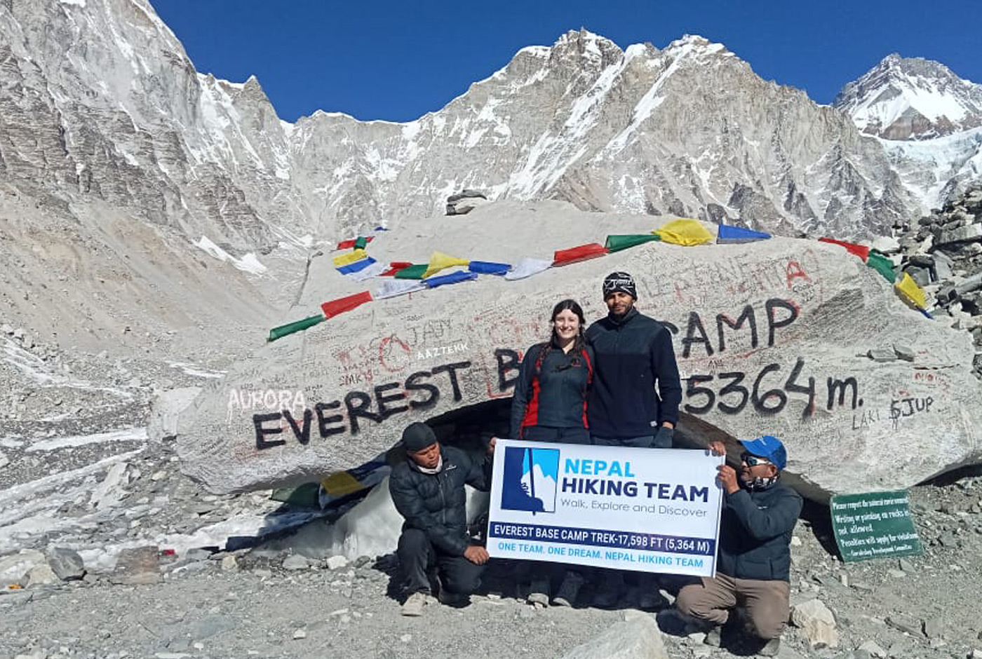 Trekkers standing at Everest Base Camp sign at 5,364m in Nepal with snow-capped Himalayan peaks