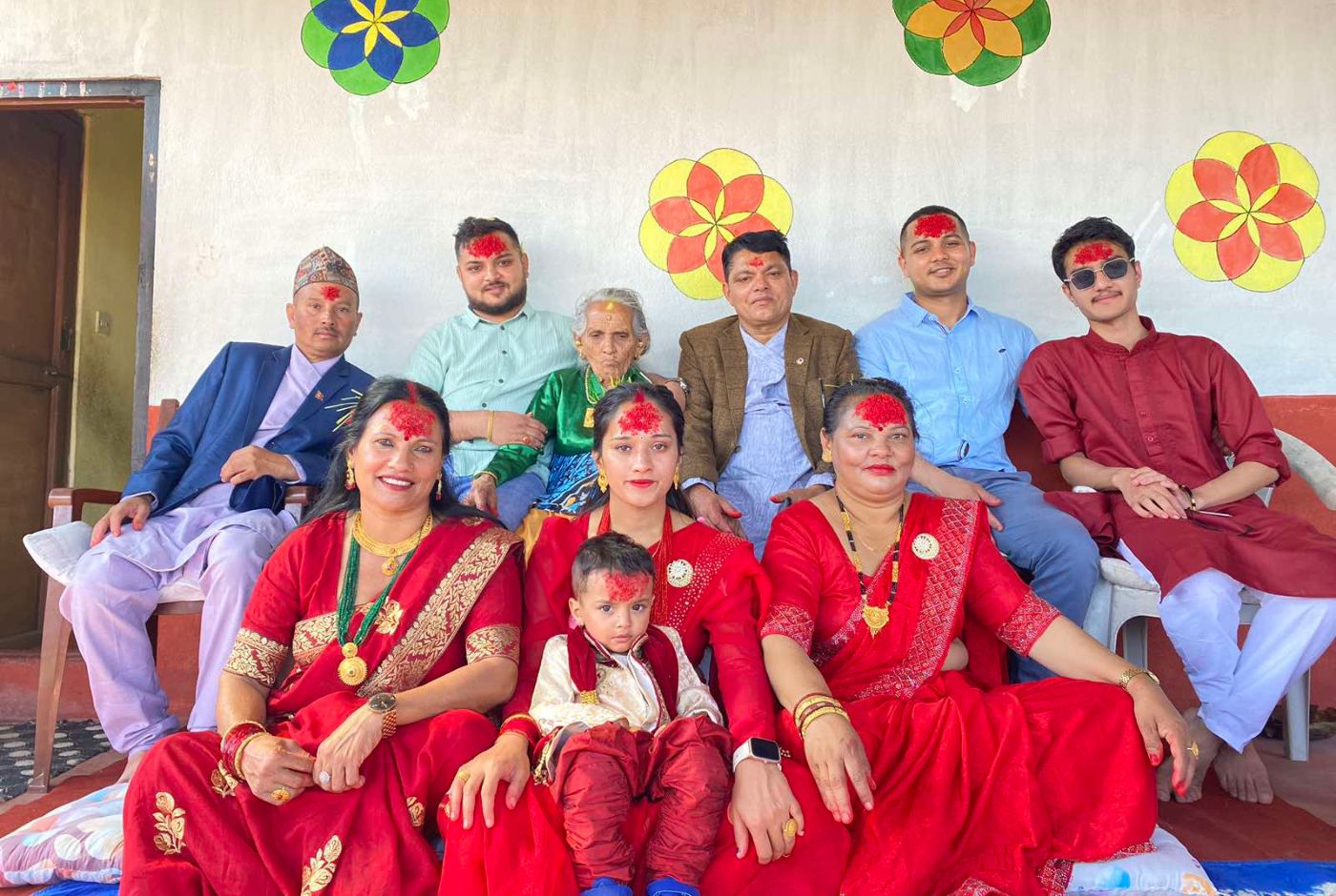 Multigenerational Nepali family seated together during Dashain, wearing traditional red clothing and tika on their foreheads.