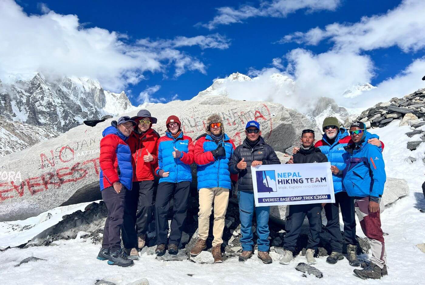 Successful trekking group at Everest Base Camp sign at 5,364 meters with Khumbu Icefall and Pumori peak backdrop