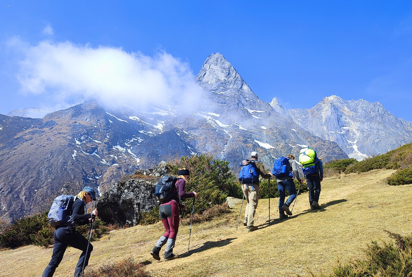 Trekkers with trekking poles ascending gradual trail to Everest View Hotel above Namche Bazaar with Ama Dablam peak behind