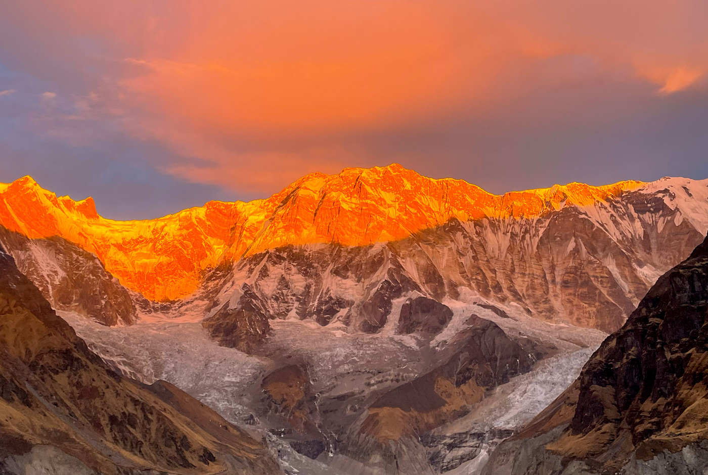 Annapurna mountain peaks illuminated by golden sunrise light with glacier visible in valley below, dramatic orange and purple sky, Annapurna Conservation Area