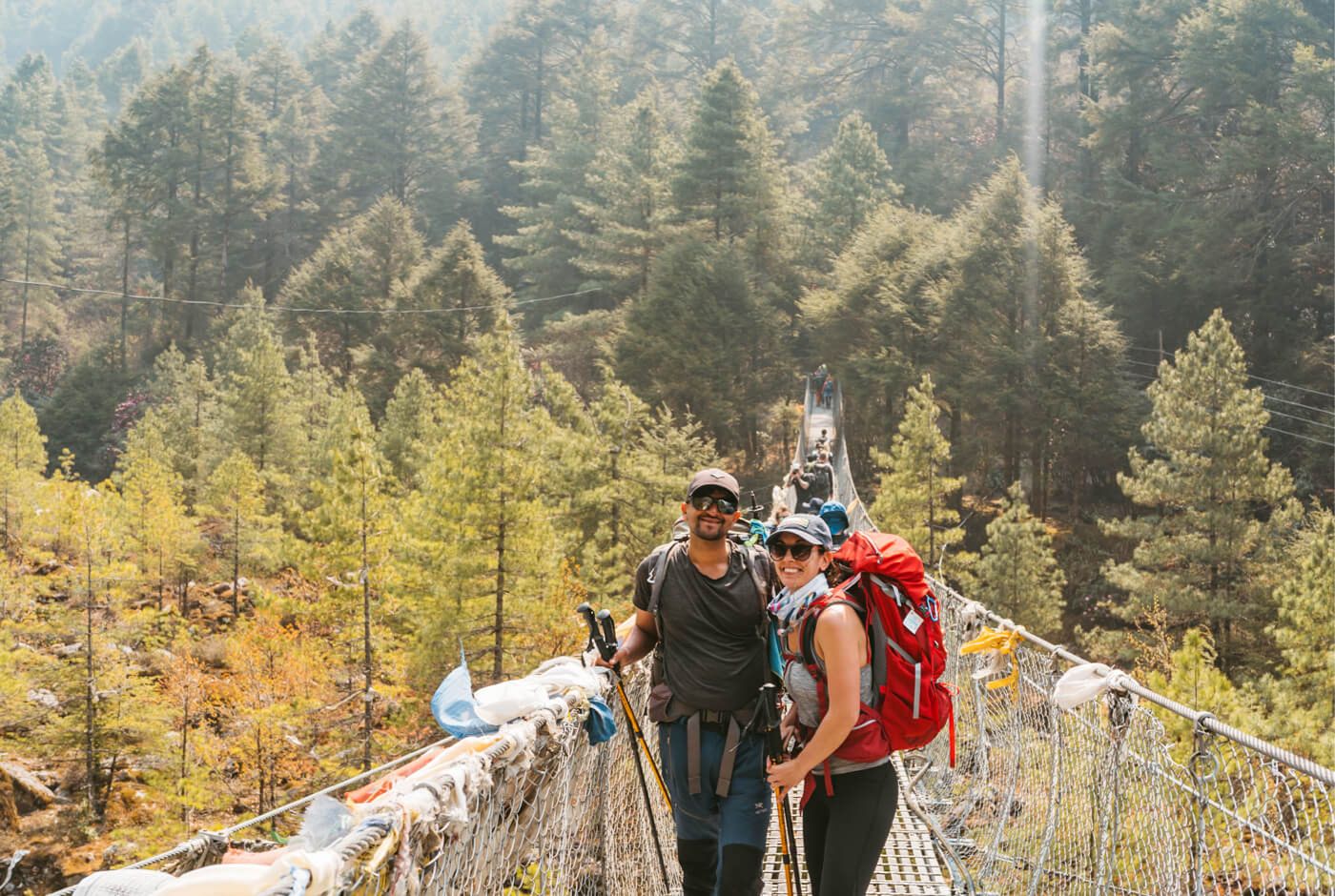 Trekkers crossing a suspension bridge on the Everest Base Camp trail, showing terrain hazards that require travel insurance coverage