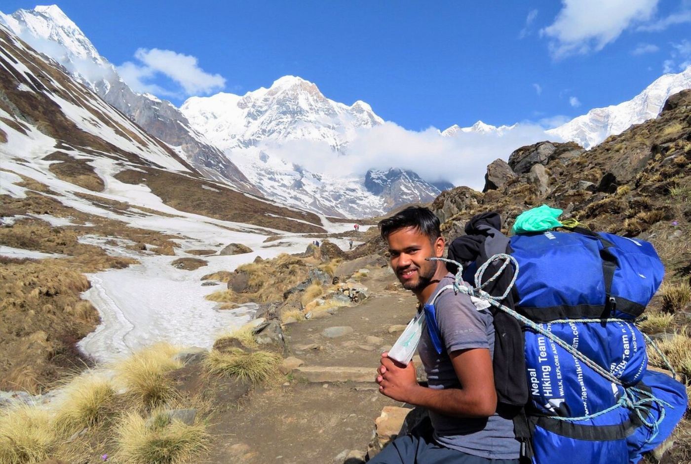 Nepal Hiking Team porter carrying trekking gear on Annapurna Base Camp trail with snowy peaks