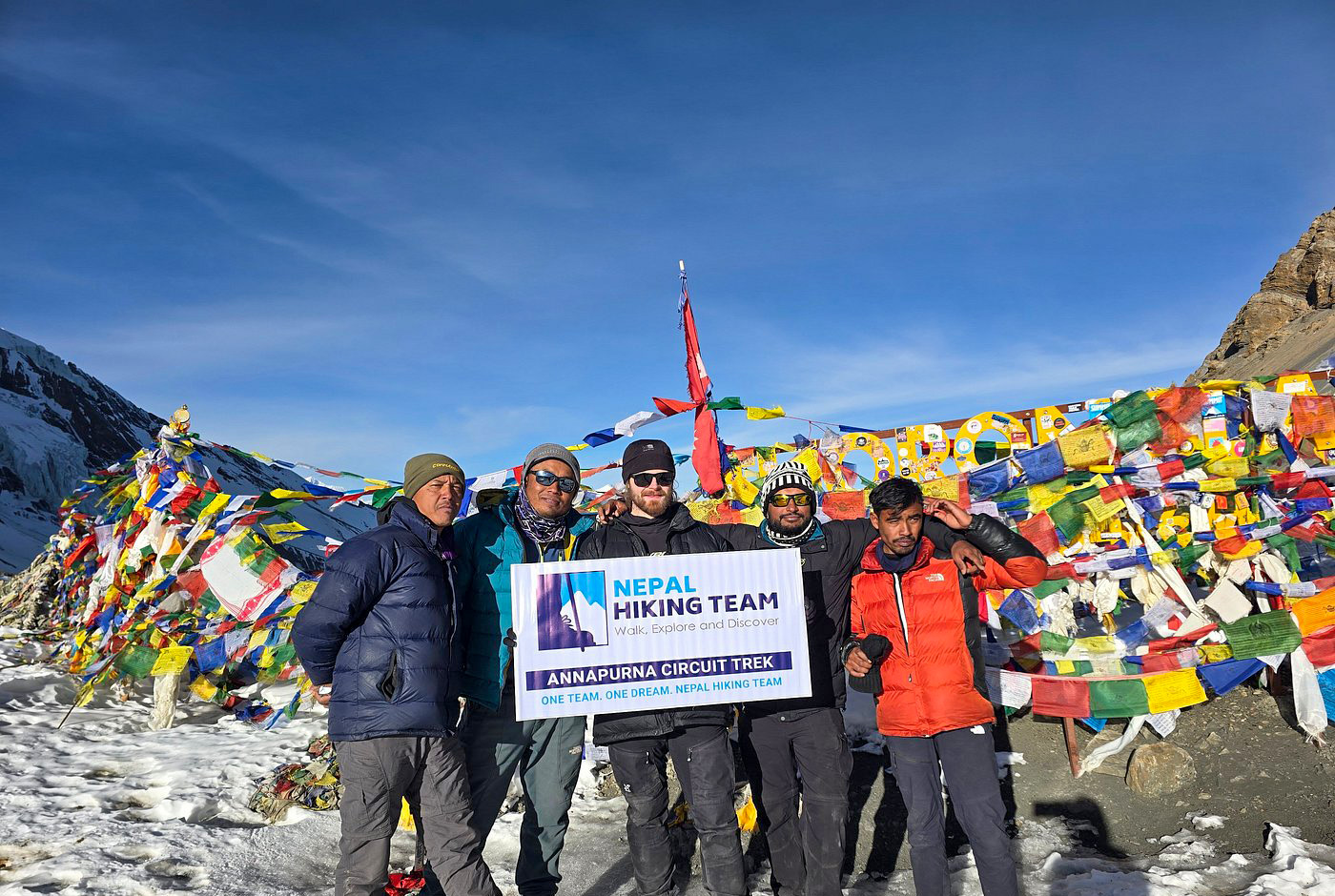 Trekkers posing at Thorong La Pass with colorful prayer flags on the Annapurna Circuit Trek, Nepal