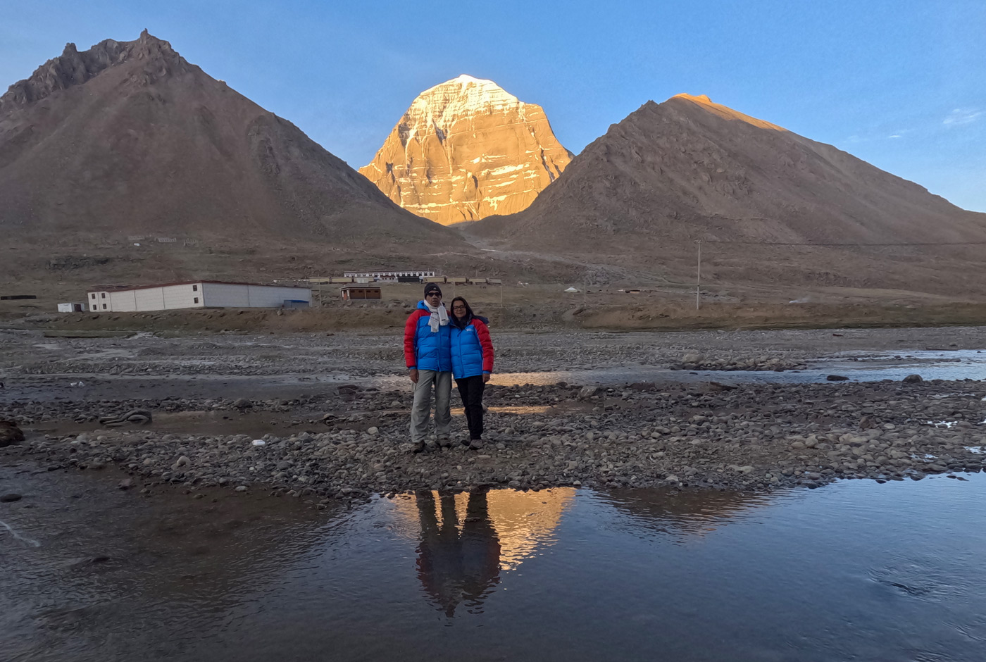North face of Mount Kailash glowing at sunrise, showing its pyramid-like shape, with travelers near its base in western Tibet