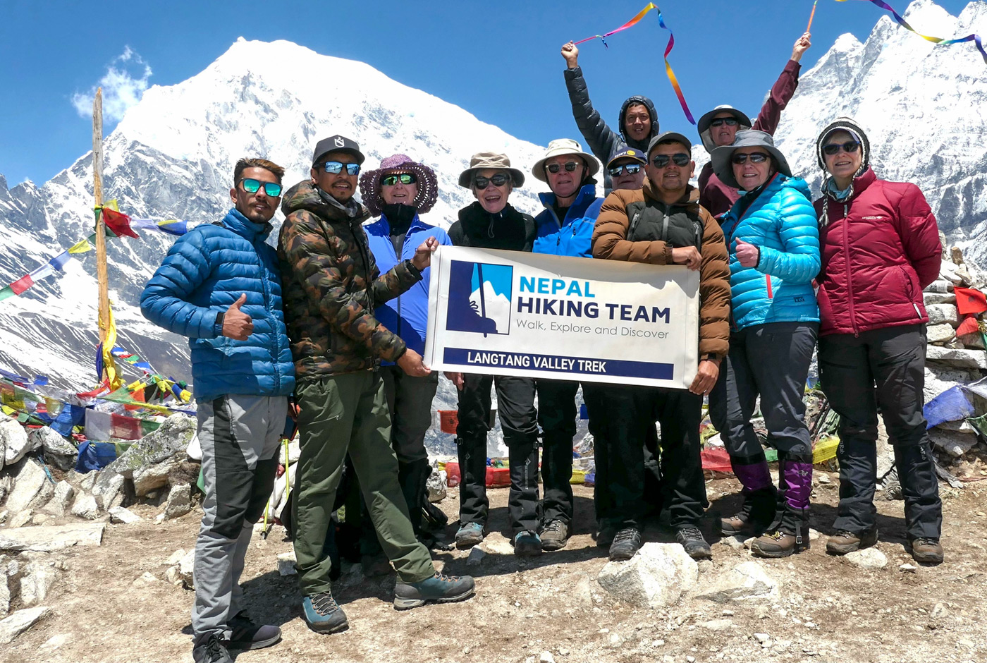 Group Of Trekkers Celebrating At Langtang Valley Viewpoint With Prayer Flags And Snow Capped Himalayan Peaks