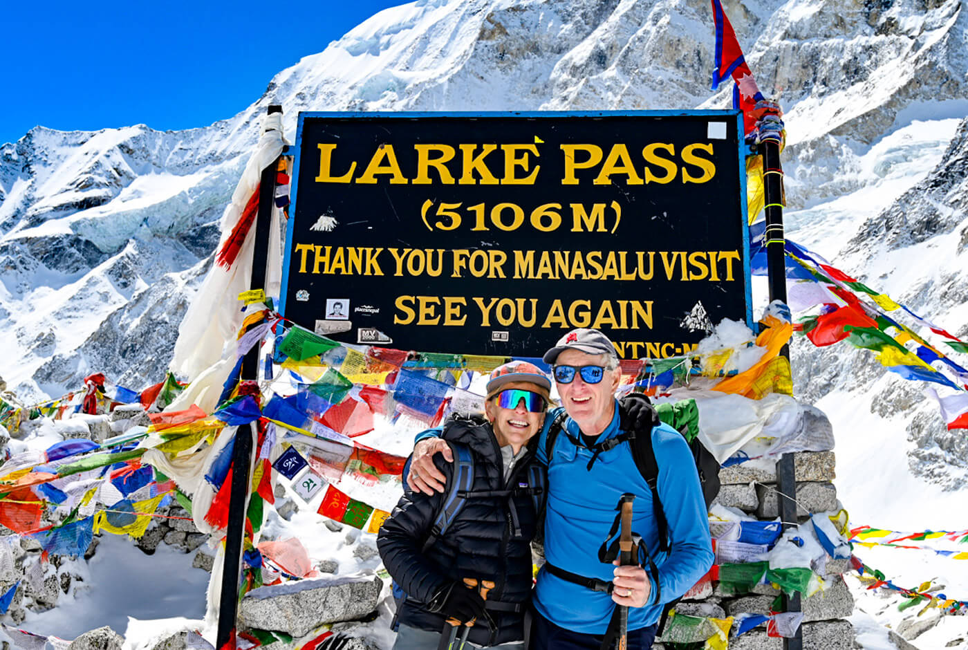 Trekkers in layered jackets, sunglasses, and trekking poles at Larkya La Pass 5106m on the Manaslu Circuit Trek &mdash; essential gear for high-altitude trekking in Nepal