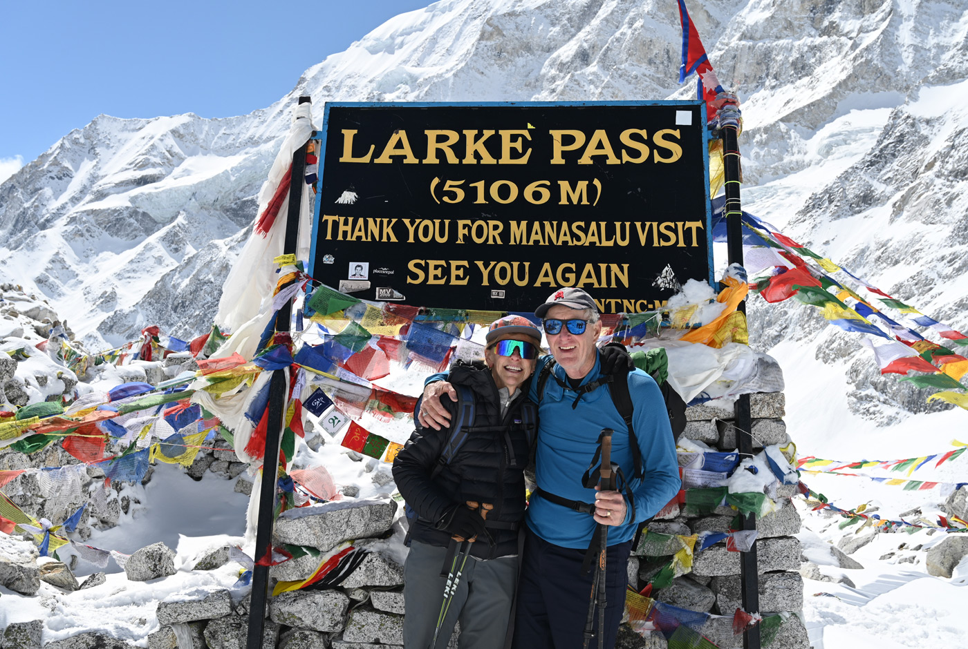Two trekkers posing at Larkya La Pass 5160m sign with prayer flags Manaslu Circuit Trek Nepal