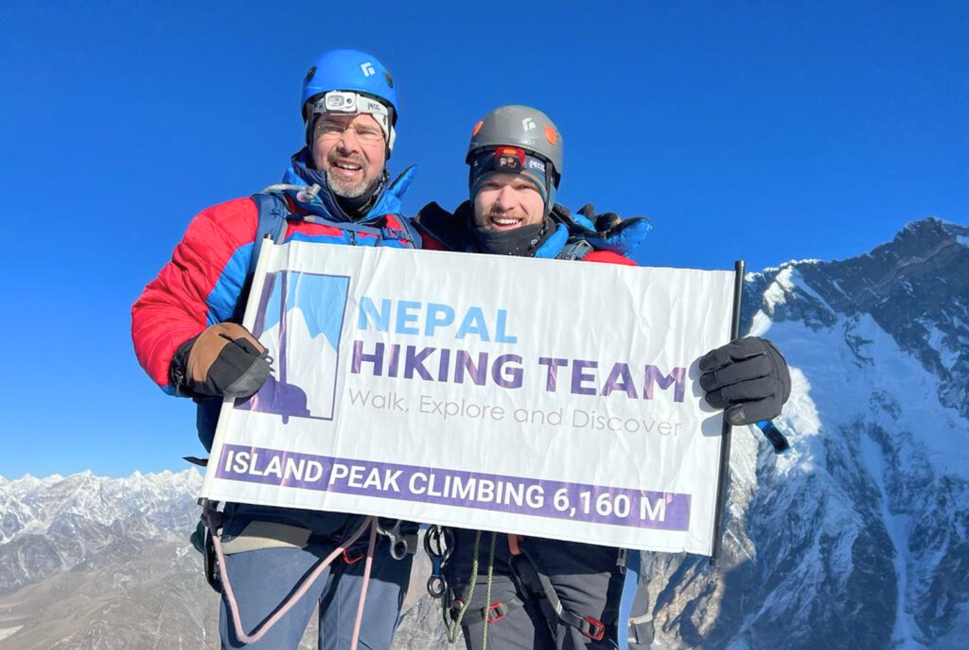 Two climbers holding a 'Nepal Hiking Team' banner at the summit of Island Peak