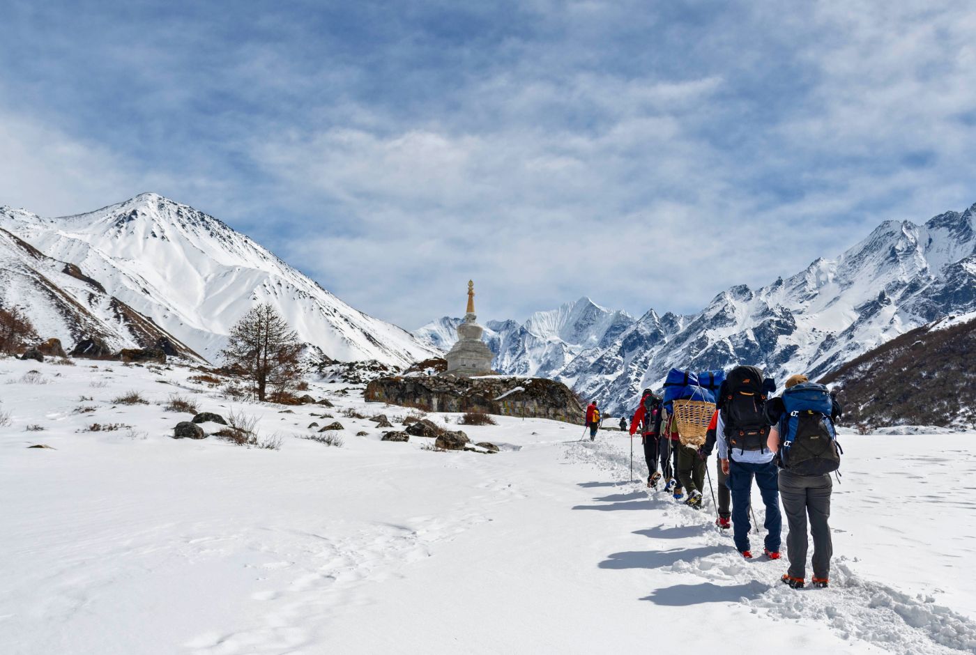 Langtang Valley winter trek group with porters and guides walking through snow toward Buddhist stupa with Himalayan peaks Nepal